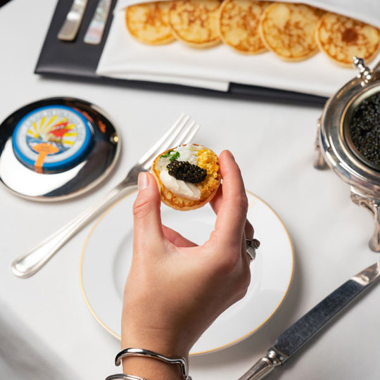 Hand picking up a bilni with caviar on top