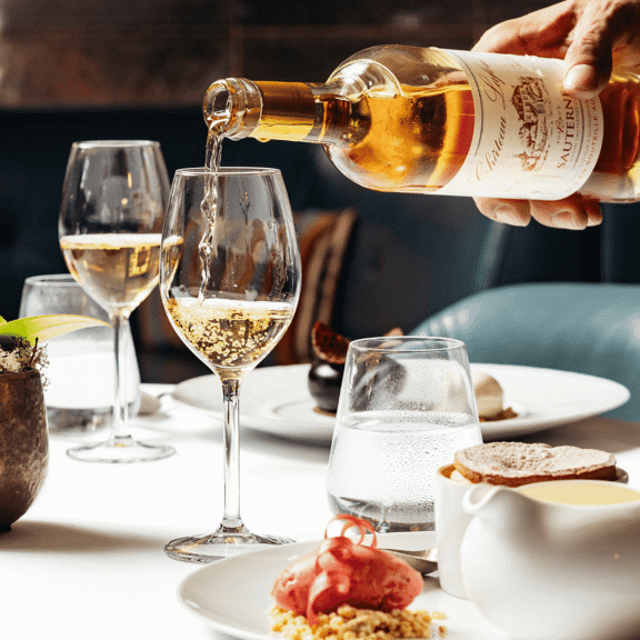 Dessert wine being poured into a wine glass on a laid table with dessert